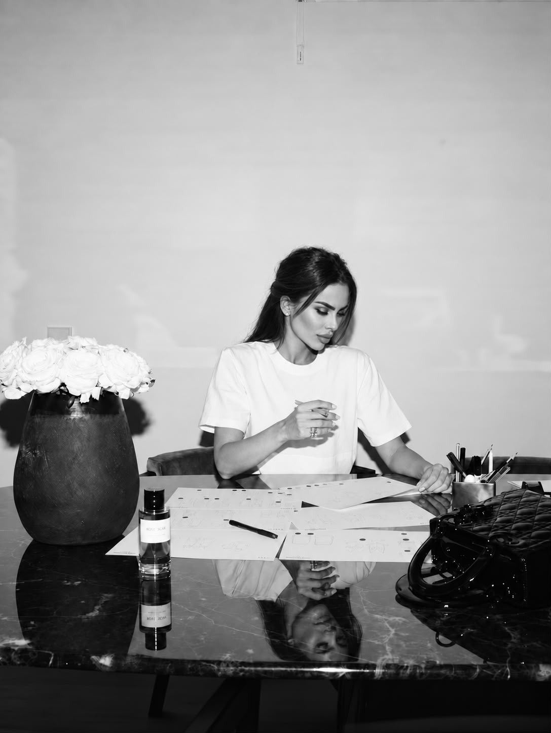 Giulia Nati alla scrivania, al lavoro su bozzetti, accanto a un vaso di rose bianche